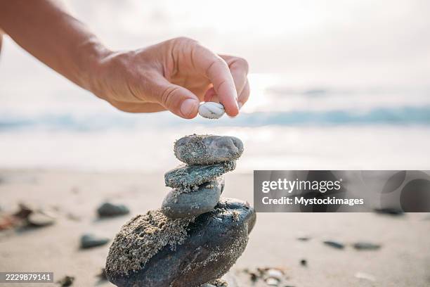 hand stacking stones on sandy beach shore - gestapelde stenen stockfoto's en -beelden
