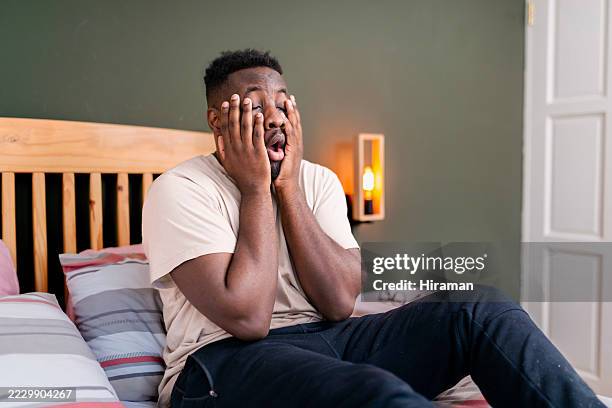 tired man sitting on bed holding face expressing fatigue and sleepiness - unexpected stock pictures, royalty-free photos & images