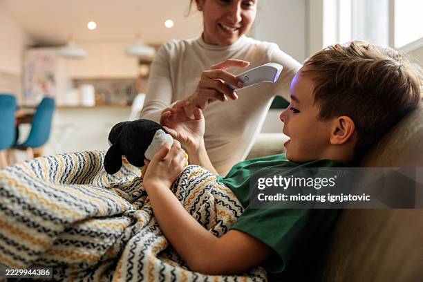 une mère utilise un thermomètre numérique pour vérifier la fièvre de son fils - thermomètre à affichage digital photos et images de collection