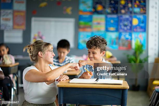 teacher encouraging student in classroom with learning activity and positive support - criança de escola primária imagens e fotografias de stock