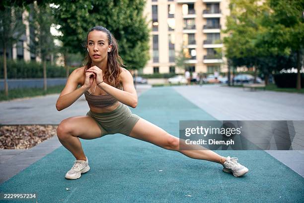 young woman performing stretching exercise outdoors on a city sports path - legs apart stock pictures, royalty-free photos & images
