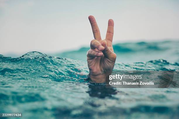 hand showing peace sign above ocean waves on a sunny day - menselijke vinger stockfoto's en -beelden