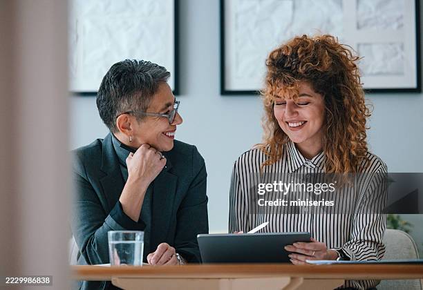 dos empresarias colaborando durante una reunión en un entorno de oficina moderno - dedicación fotografías e imágenes de stock