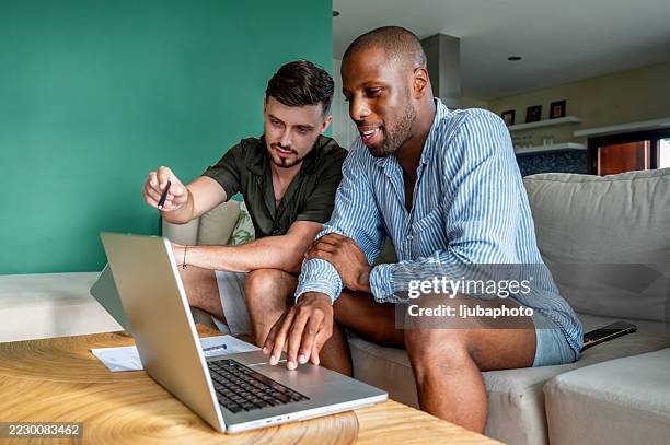 deux amis collaborent sur un projet à l’aide d’un ordinateur portable à la maison - masculinité moderne photos et images de collection