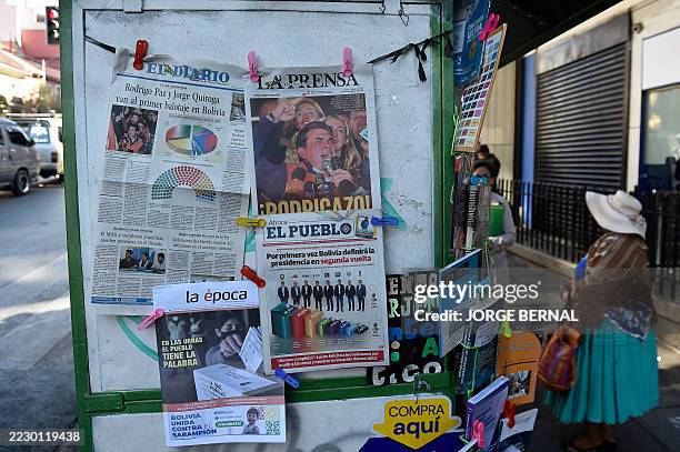 Woman stands next to a kiosk displaying newspapers with front-page coverage of Bolivia's presidential election, in La Paz, on August 18, 2025. A...