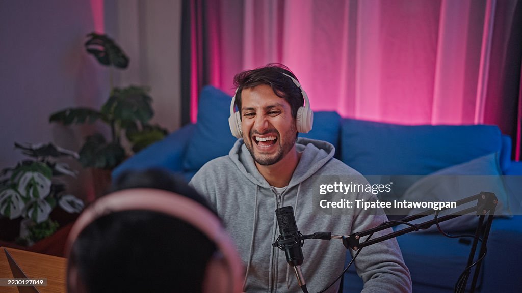 Young male and female podcasters wear headphones speaking in microphone and interview sit at desk with laptop at studio. Streaming live podcast concept.