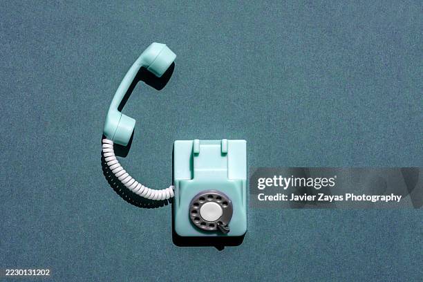 light blue vintage dial telephone resting on a dark turquoise surface - telephone receiver stock pictures, royalty-free photos & images