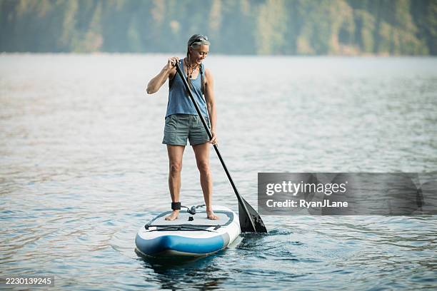 mature woman paddleboarding - paddleboard stock pictures, royalty-free photos & images