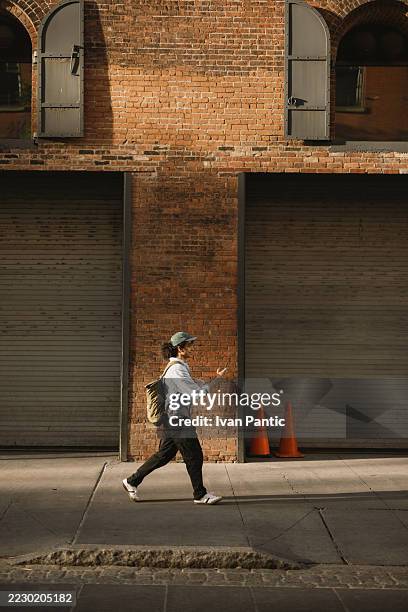 young man walking on the sidewalk and using his smartphone - side wall stock pictures, royalty-free photos & images
