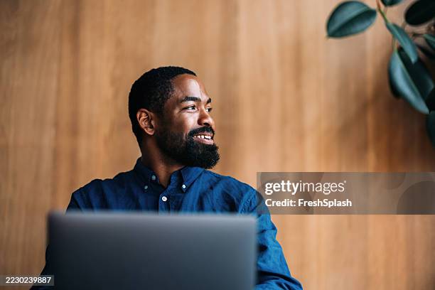 hombre profesional sonriendo trabajando en una computadora portátil en un entorno de oficina moderno - vestimenta casual fotografías e imágenes de stock