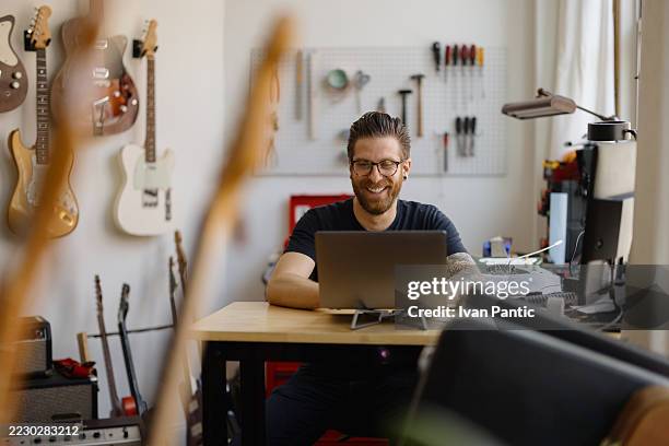 luthier souriant et travaillant sur ordinateur portable dans son atelier - représentation masculine photos et images de collection