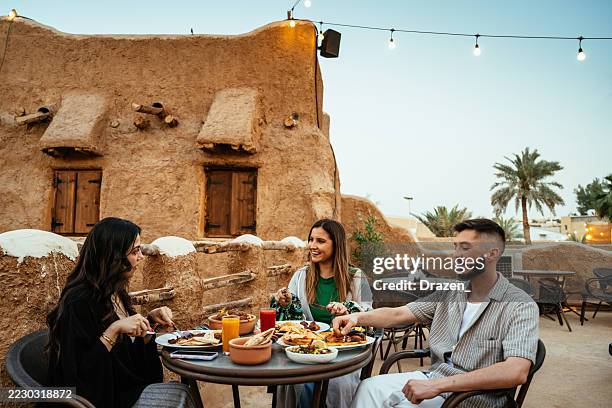 rooftop restaurant setting with diverse people enjoying a meal, featuring traditional middle eastern clothing and architecture. - medina district stock pictures, royalty-free photos & images