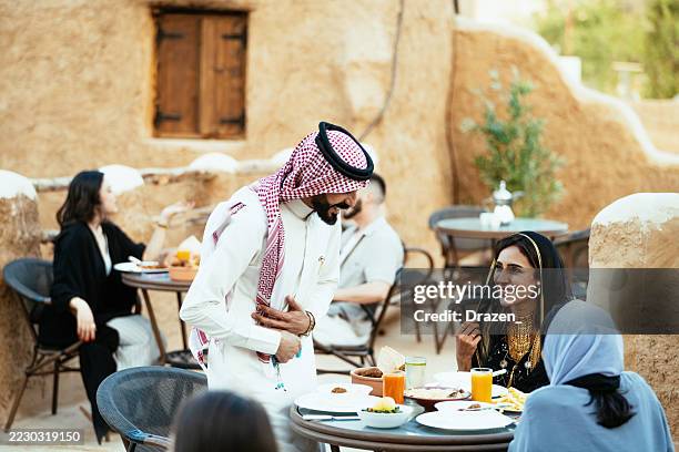 outdoor restaurant setting with diverse people enjoying a meal, featuring traditional middle eastern clothing and architecture. - medina district stock pictures, royalty-free photos & images