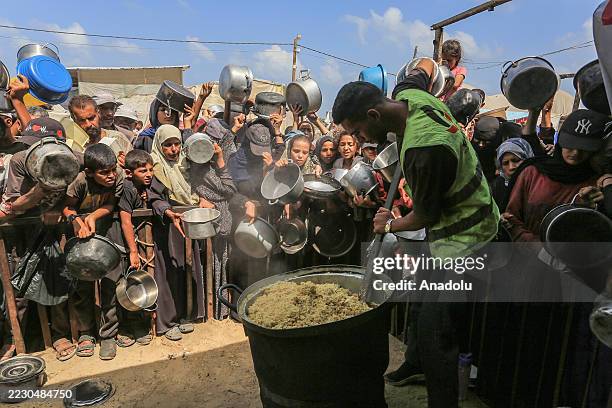 Palestinians, including children, who are struggling to access food due to Israel's blockade and ongoing attacks on the Gaza Strip, wait in line to...