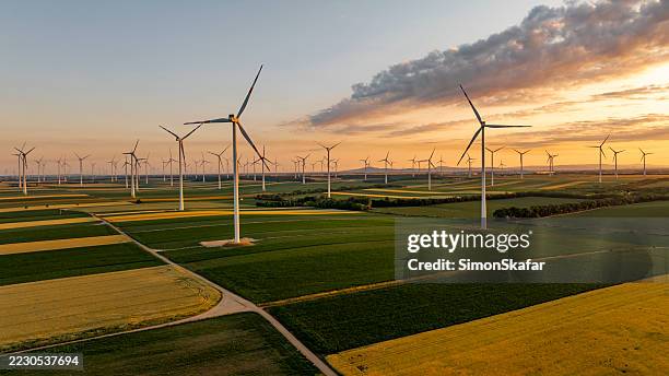 tramonto sulle turbine eoliche in vasti campi agricoli con colture dorate e verdi - mulino a vento foto e immagini stock