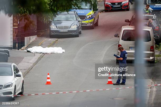 August 2025, North Rhine-Westphalia, Menden: Police forensics investigators are working at the crime scene; the covered body of a person who has been...