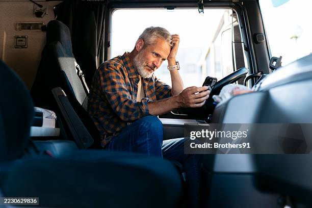 worried truck driver reading bad news on mobile phone inside cabin - truck driver stock pictures, royalty-free photos & images