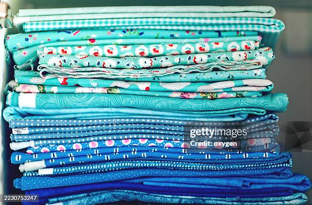 stack of folded blue and aqua fabrics. neatly folded fabrics in shades of blue and aqua with patterns, stacked in a colorful textile pile. - haberdashery stock pictures, royalty-free photos & images