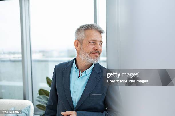 confident middle-aged man in formal attire looking thoughtfully out a window - high contrast stock pictures, royalty-free photos & images