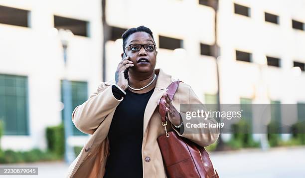 black woman walking in city, talking on mobile phone - shoulder bag stock pictures, royalty-free photos & images