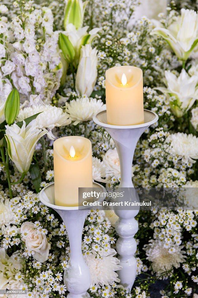 Beautiful white floral arrangement with two cream-colored LED candles on elegant white candle holders