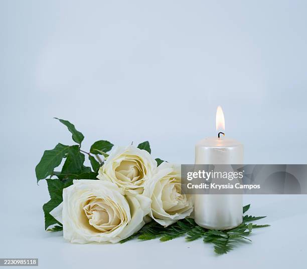 white candle and three roses on white background - memorial event stock pictures, royalty-free photos & images