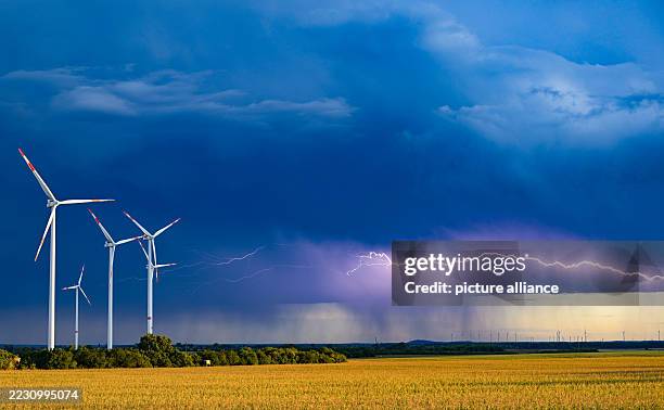 August 2025, Brandenburg, Sieversdorf: Lightning from a thunderstorm shines against dark clouds over a wind farm. Photo: Patrick Pleul/dpa