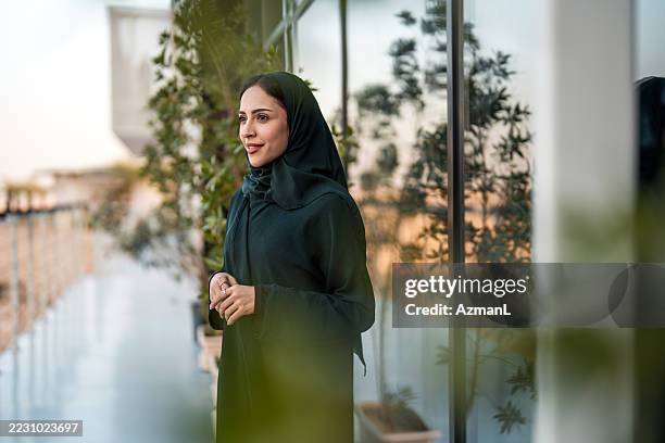 confident young middle eastern businesswoman in black hijab standing on modern office balcony - saudi arabia woman stock pictures, royalty-free photos & images