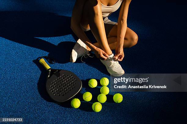female athlete tying shoelaces next to paddle racket on blue court - tennisbal stockfoto's en -beelden