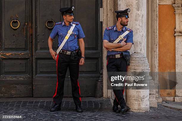 Two Carabinieri officers wearing their summer uniform: a peaked cap, short sleeved blue shirt, flat black shoes and black trousers bearing the...