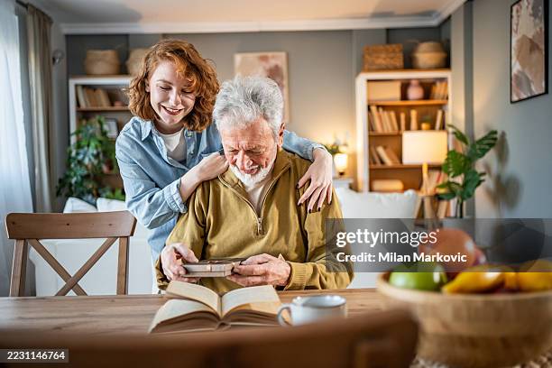 nipote che abbraccia il nonno che legge il libro a casa - nostalgia foto e immagini stock
