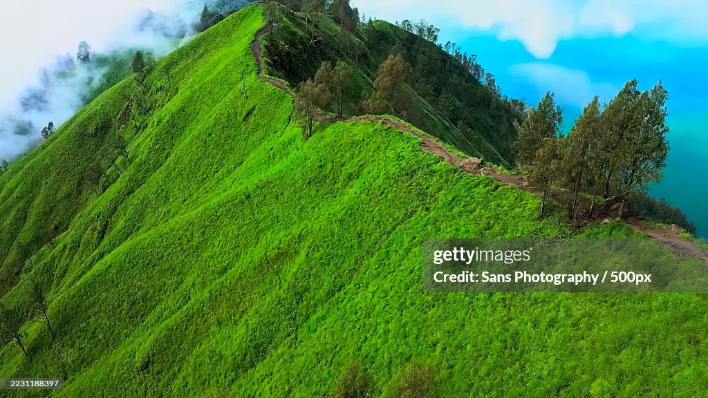 Lush Green Hillside with Misty Clouds and Blue Sky
