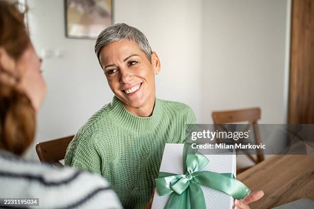 femme adulte moyenne offrant un cadeau à un ami à la maison - donner photos et images de collection