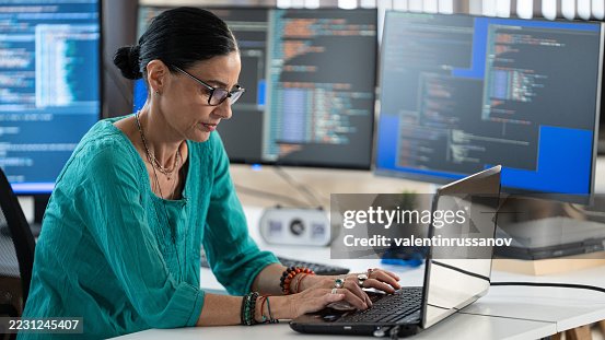 Senior Female Software Developer Coding in Modern Tech Office with Multiple Monitors. Software developer, artificial intelligence and programming. Senior Female Software Developer Coding in Modern Tech Office with Multiple Monitors. Software developer, artificial intelligence and programming.