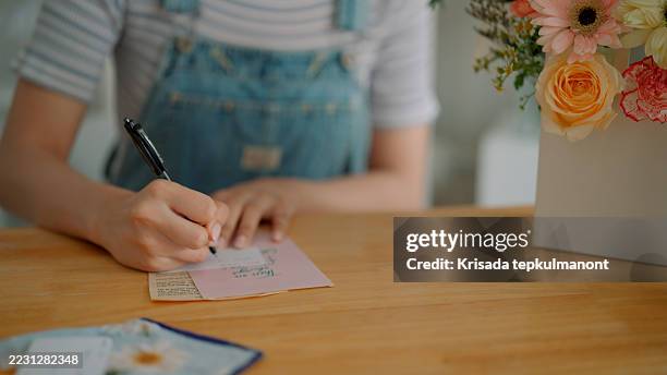 female florist writing gift tag for customer before attaching it to flower arrangement. - gift shop stock pictures, royalty-free photos & images