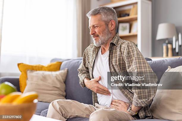 man holding his stomach in pain while resting on the couch. - människans matsmältningsorgan bildbanksfoton och bilder