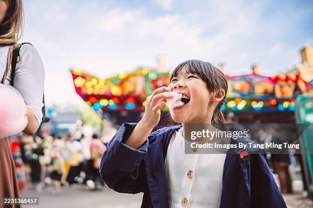 child eating cotton candy at colourful street fair with parent - amusement park stock pictures, royalty-free photos & images