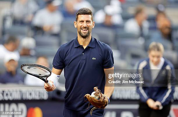 Tennis player Novak Djokovic has a laugh carrying his tennis racquet before throwing the ceremonial first pitch prior to a game between the New York...