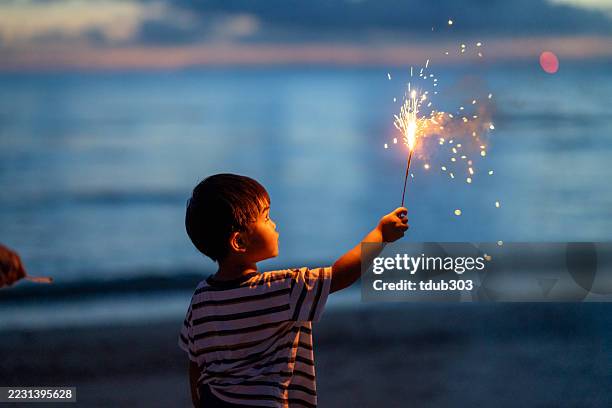 young boy holding a firework on a beach with relaxed emotions - sparkler stock pictures, royalty-free photos & images