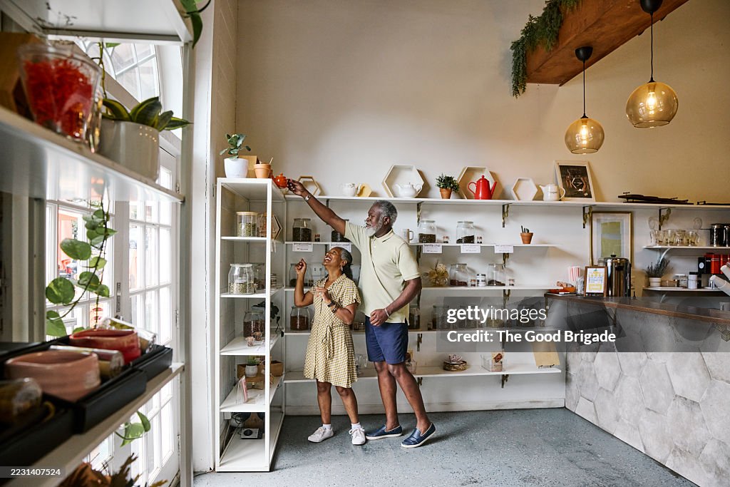Man helping female friend in removing teapot from shelf