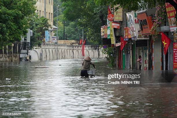 Woman pushes her bicycle through a flooded street following the passage of Typhoon Kajiki in Hanoi on August 26, 2025. Vietnam evacuated tens of...