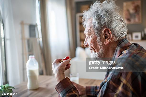 älterer mann genießt zu hause einen cracker mit marmelade und milch - einzelner senior stock-fotos und bilder