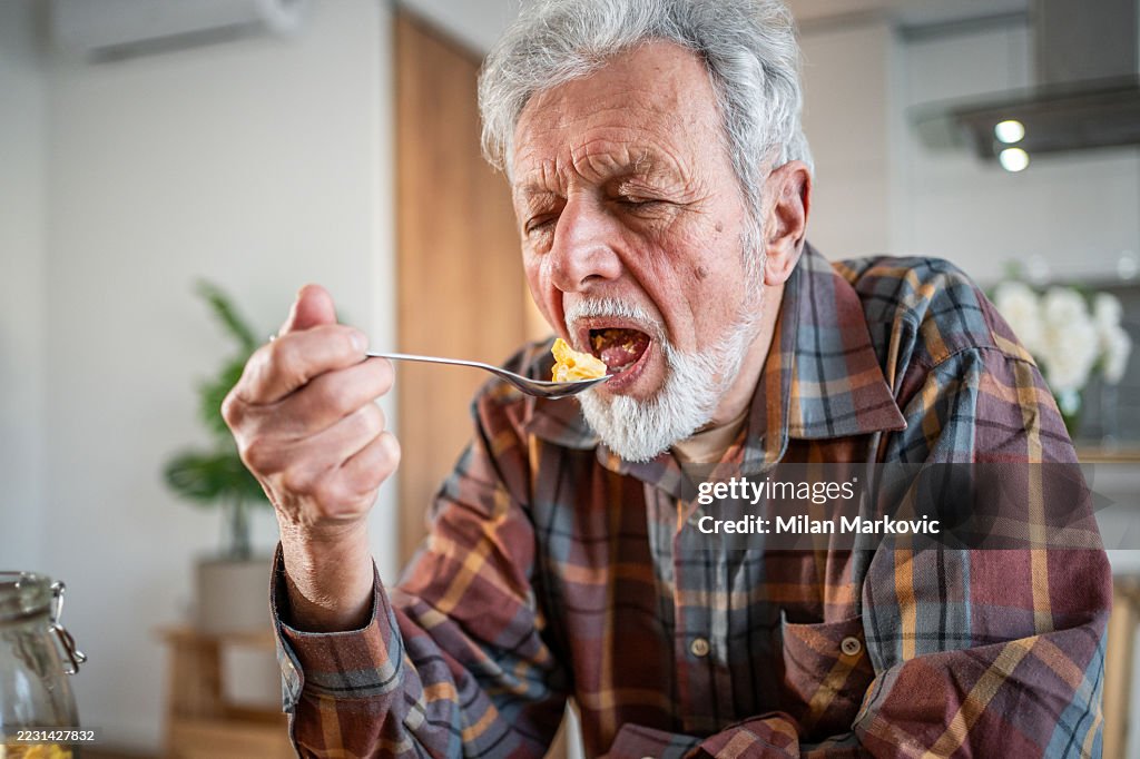 Senior man eating food with difficulty at home