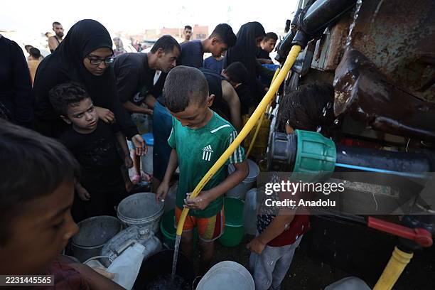 Palestinians displaced in Gaza City are viewed trying to meet their daily water needs by filling jerry cans with water distributed by tankers in the...