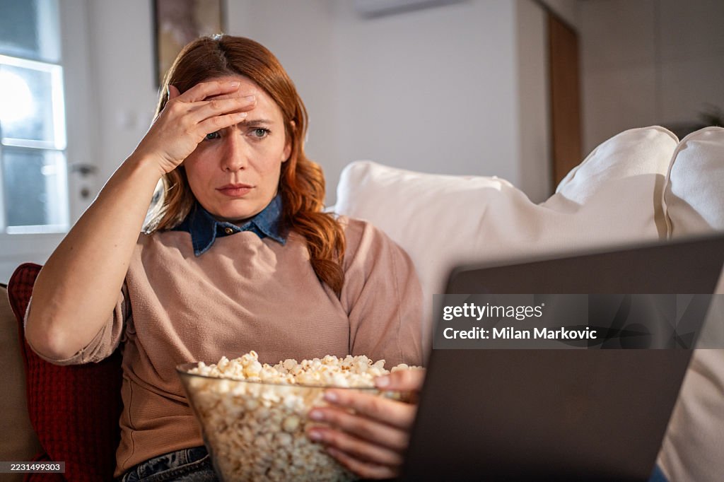 Mulher estressada assistindo a um filme no laptop enquanto come pipoca