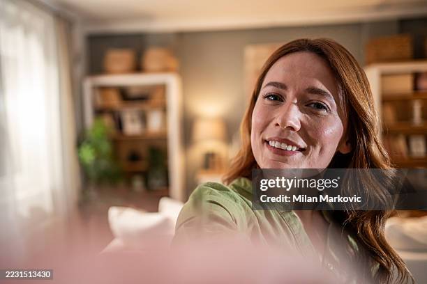 young woman making a selfie at home smiling at the camera - kleine scherptediepte stockfoto's en -beelden