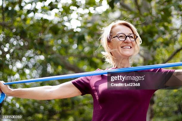 mujer rubia madura haciendo ejercicios con una banda elástica en el parque de la ciudad - goma elástica fotografías e imágenes de stock