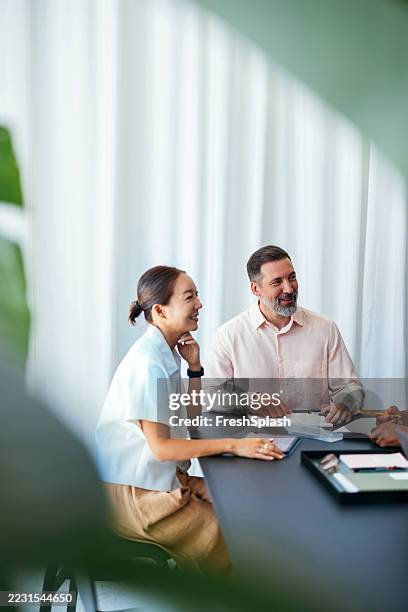 colegas profesionales sonriendo y discutiendo tareas durante una reunión de negocios - colega fotografías e imágenes de stock