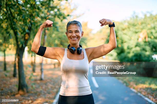 mujer adulta mayor mostrando sus bíceps mientras hace ejercicio al aire libre - flexionar los músculos fotografías e imágenes de stock