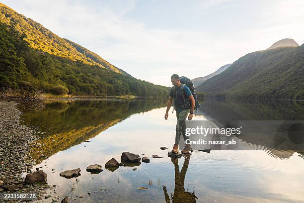 adventurer crossing stream by stepping on rocks. - stepping stone stock pictures, royalty-free photos & images
